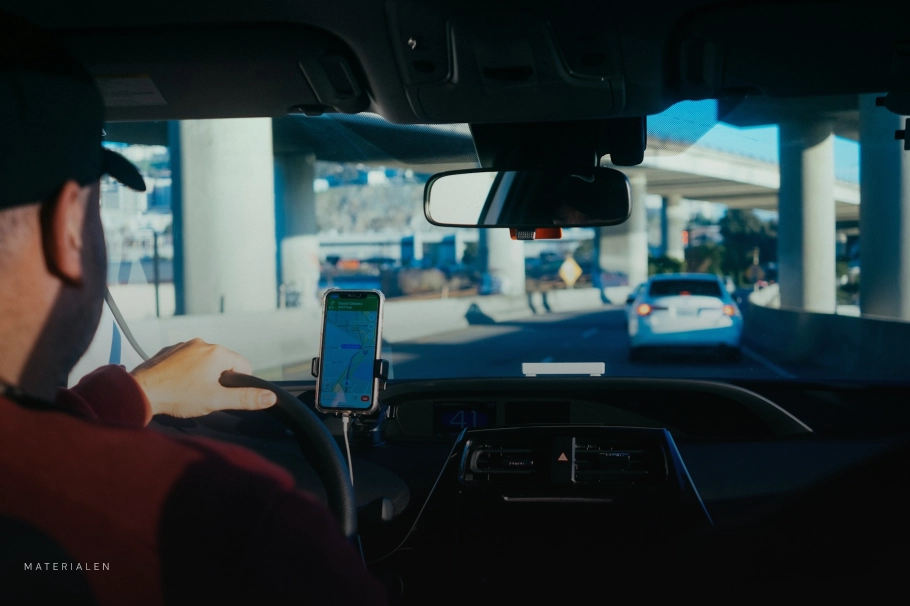 Uitzicht van binnenuit een auto waarin een man rijdt en een smartphone op het dashboard gebruikt voor GPS-navigatie op de snelweg